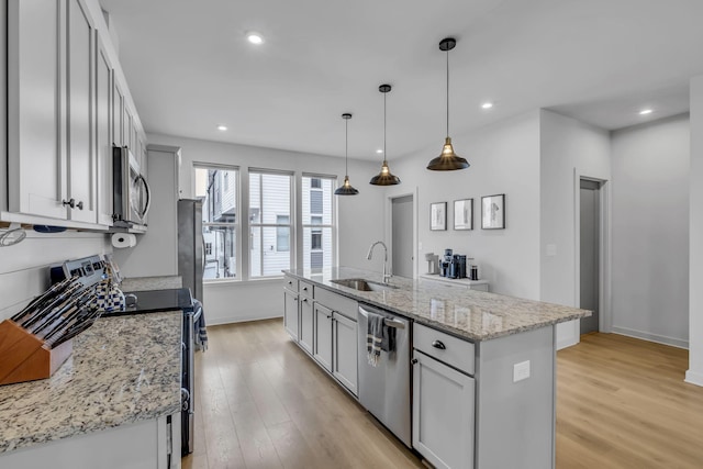 kitchen with pendant lighting, sink, a kitchen island with sink, stainless steel appliances, and light stone countertops