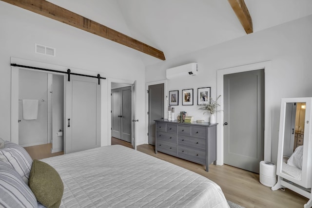 bedroom featuring beam ceiling, a wall unit AC, a barn door, and light wood-type flooring