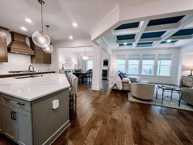 kitchen with decorative light fixtures, a center island with sink, dark wood-type flooring, and premium range hood