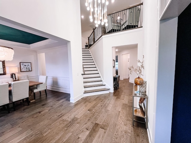 entryway featuring hardwood / wood-style flooring, crown molding, a chandelier, and a high ceiling