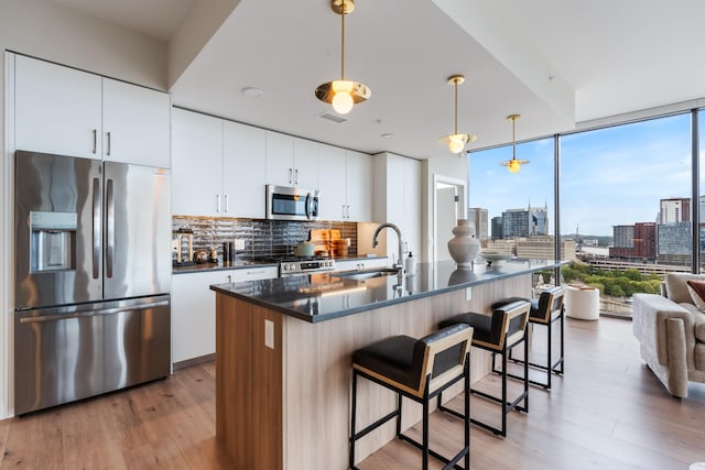 kitchen featuring sink, a center island with sink, appliances with stainless steel finishes, pendant lighting, and white cabinets