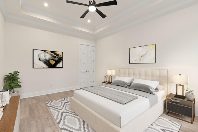 bedroom with light hardwood / wood-style flooring, ceiling fan, ornamental molding, a raised ceiling, and a closet