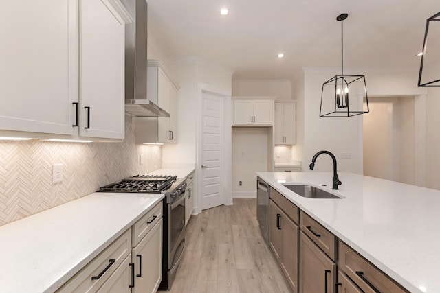 kitchen featuring white cabinetry, sink, hanging light fixtures, stainless steel appliances, and wall chimney range hood