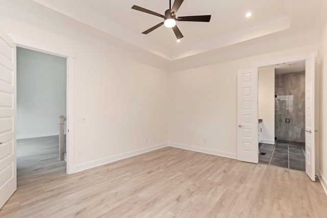 unfurnished bedroom with ceiling fan, ensuite bathroom, a raised ceiling, and light hardwood / wood-style flooring