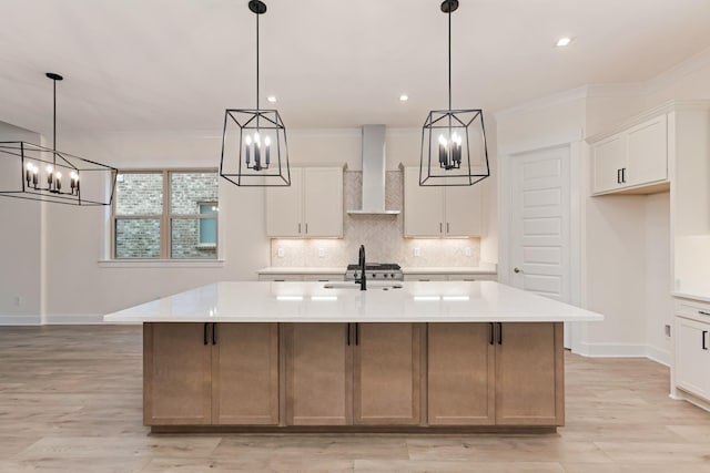 kitchen featuring white cabinetry, pendant lighting, wall chimney exhaust hood, and a large island with sink