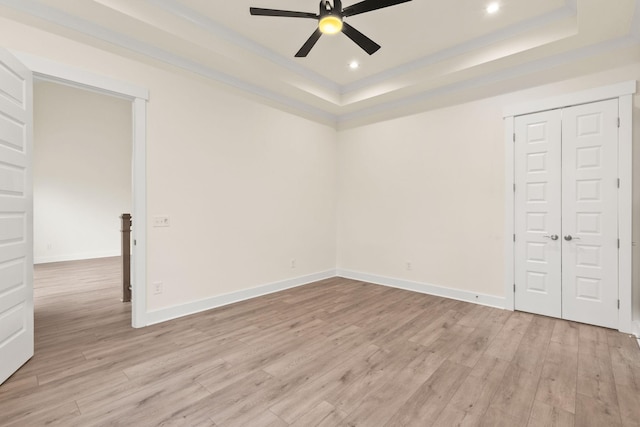 empty room featuring a raised ceiling, ceiling fan, and light wood-type flooring