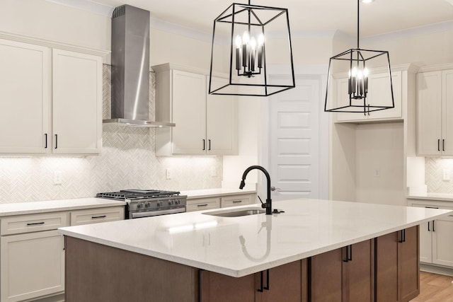 kitchen with a kitchen island with sink, wall chimney range hood, stainless steel stove, and light stone counters