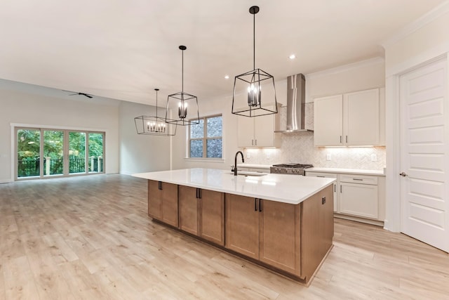 kitchen with a spacious island, wall chimney exhaust hood, sink, decorative light fixtures, and white cabinets