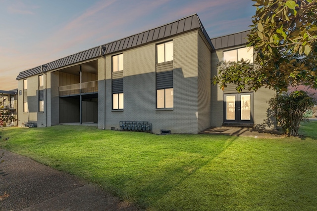 back house at dusk featuring a lawn and french doors