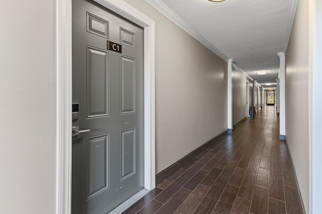 hall with dark wood-type flooring, ornamental molding, and a textured ceiling