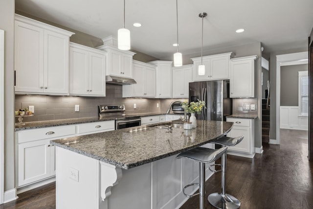 kitchen with sink, a kitchen island with sink, white cabinetry, hanging light fixtures, and stainless steel appliances