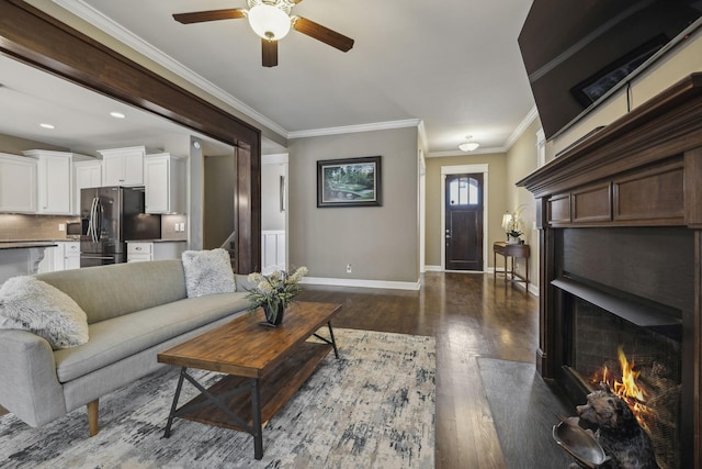 living room with crown molding, dark wood-type flooring, ceiling fan, and a fireplace