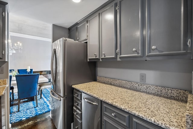 kitchen with gray cabinets, stainless steel refrigerator, ornamental molding, a notable chandelier, and light stone counters