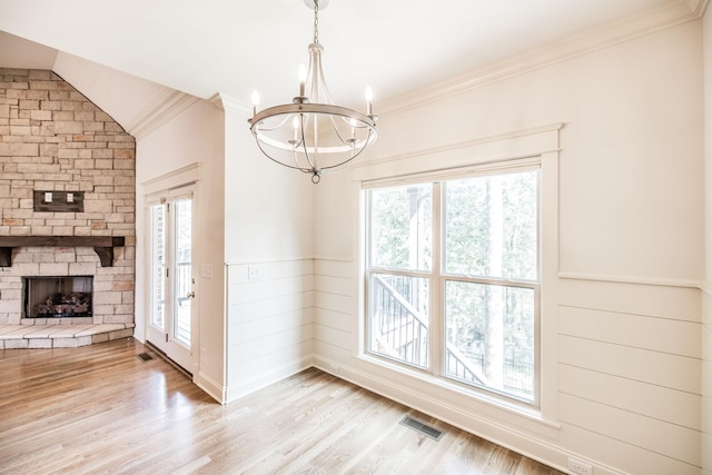 unfurnished dining area featuring crown molding, a fireplace, visible vents, light wood-style flooring, and vaulted ceiling