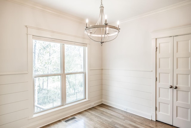 empty room with a notable chandelier, ornamental molding, visible vents, and light wood-style floors