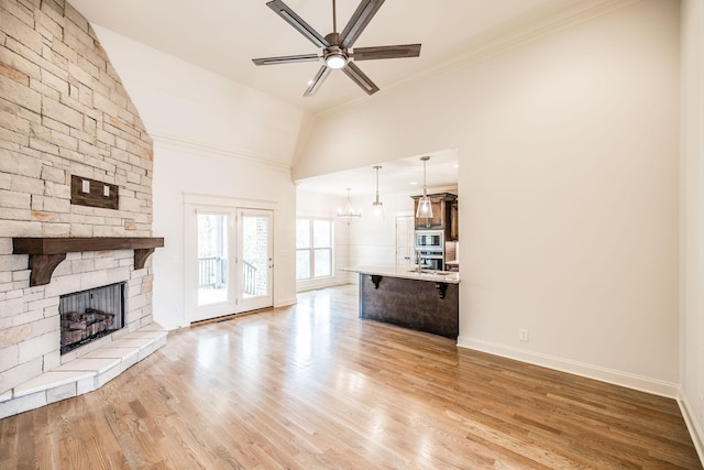 unfurnished living room with light wood finished floors, lofted ceiling, a ceiling fan, a stone fireplace, and baseboards