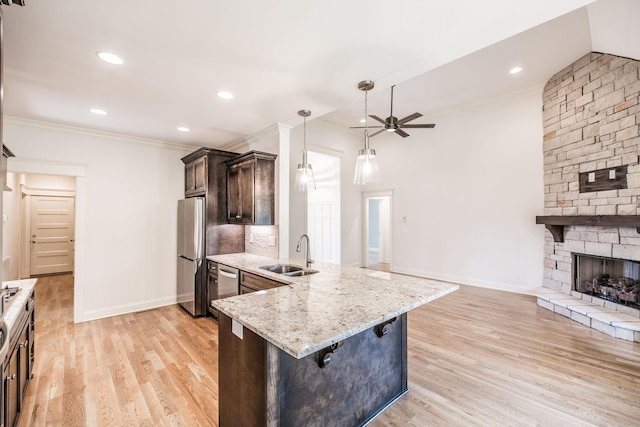 kitchen featuring dark brown cabinetry, ornamental molding, stainless steel appliances, a stone fireplace, and a sink