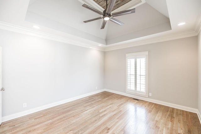 empty room featuring light wood-style flooring, a ceiling fan, baseboards, a raised ceiling, and crown molding