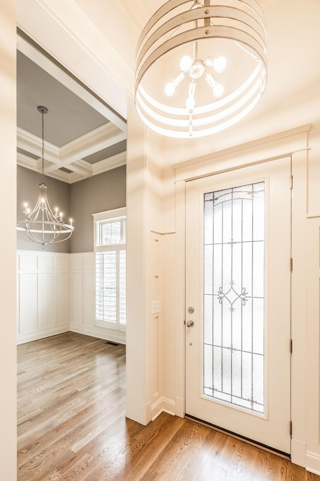 entrance foyer with a chandelier, coffered ceiling, wood finished floors, and crown molding