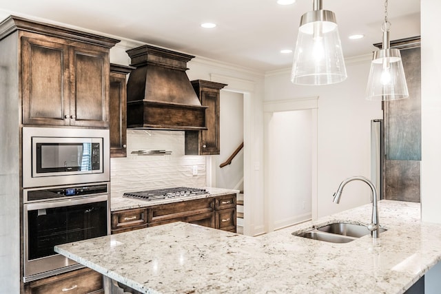 kitchen featuring dark brown cabinetry, custom range hood, appliances with stainless steel finishes, crown molding, and a sink