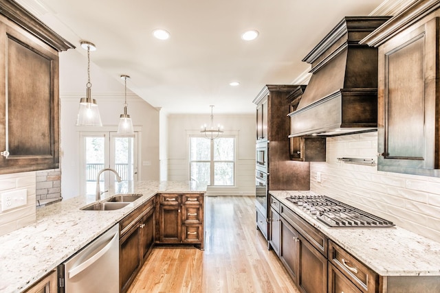 kitchen with light stone counters, custom exhaust hood, stainless steel appliances, light wood-style floors, and a sink