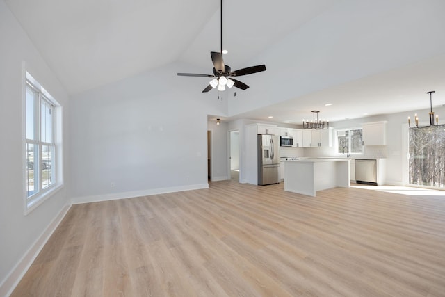 unfurnished living room featuring a sink, a wealth of natural light, ceiling fan with notable chandelier, and light wood-style floors