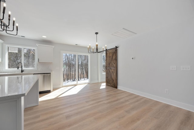 unfurnished dining area featuring a barn door, a sink, baseboards, light wood finished floors, and an inviting chandelier