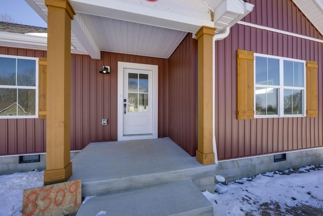 snow covered property entrance featuring board and batten siding, visible vents, and crawl space