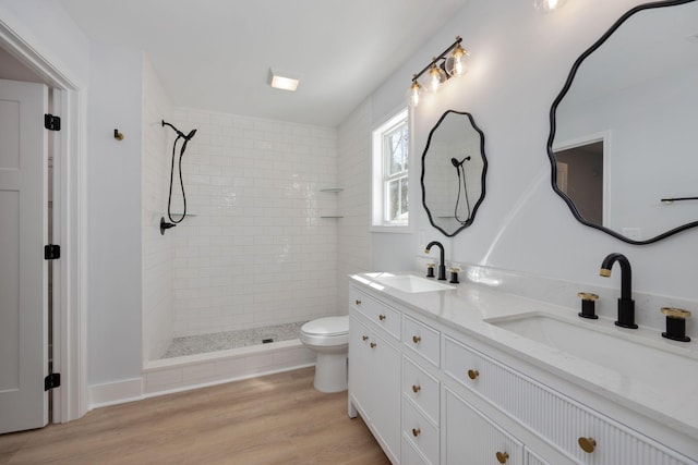 bathroom featuring double vanity, toilet, a tile shower, and a sink