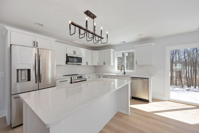 kitchen with a center island, tasteful backsplash, white cabinetry, stainless steel appliances, and light wood-style flooring
