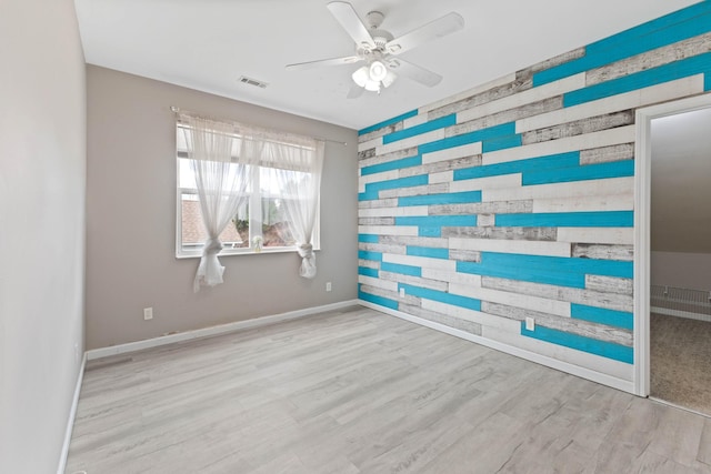 spare room featuring light hardwood / wood-style floors, ceiling fan, and wood walls