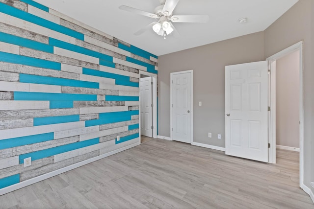 spare room with ceiling fan, light wood-type flooring, and wooden walls