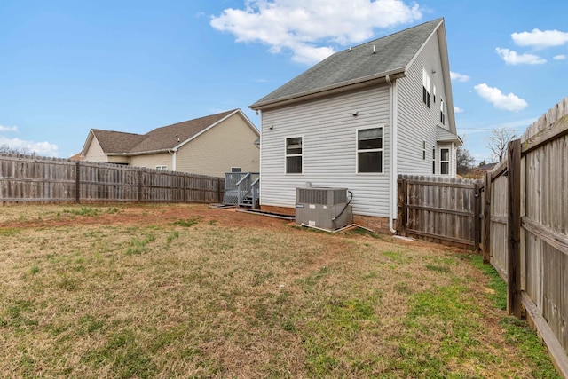 rear view of house with central AC unit and a lawn