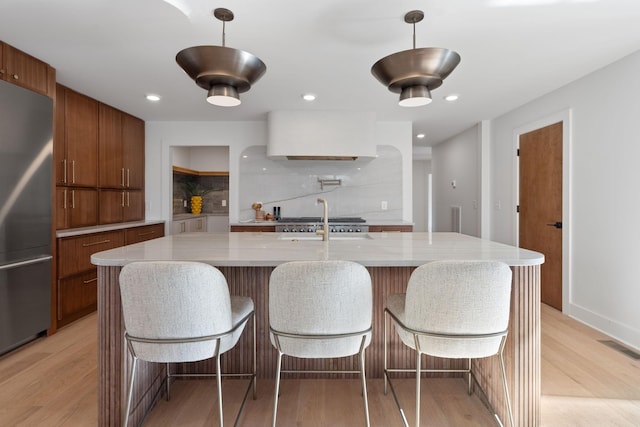 kitchen featuring decorative light fixtures, light hardwood / wood-style flooring, stainless steel appliances, and an island with sink