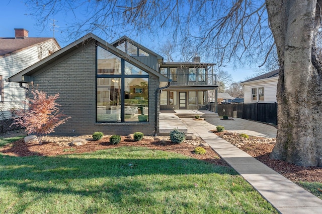 view of front facade with a balcony, a patio area, and a front lawn