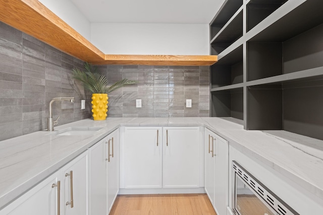 kitchen with light stone counters, sink, white cabinetry, and backsplash