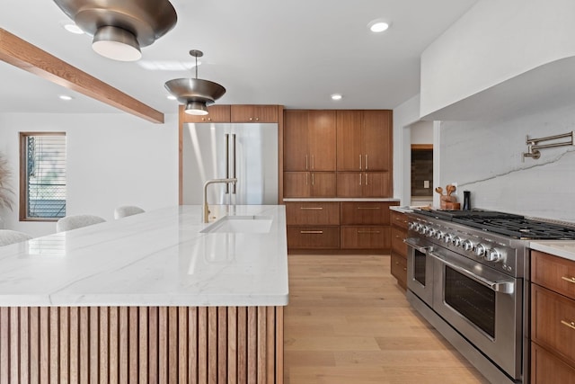 kitchen with high quality appliances, sink, light hardwood / wood-style flooring, and a large island with sink