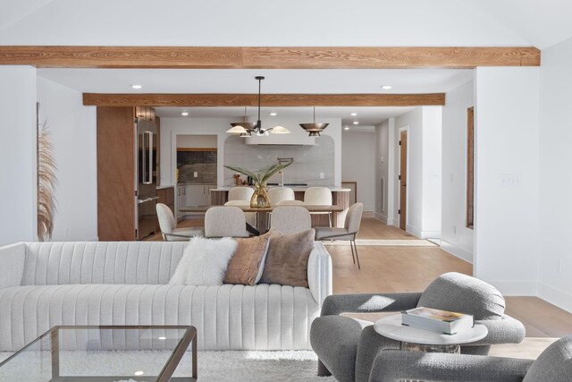 living room featuring an inviting chandelier, beam ceiling, and light hardwood / wood-style flooring