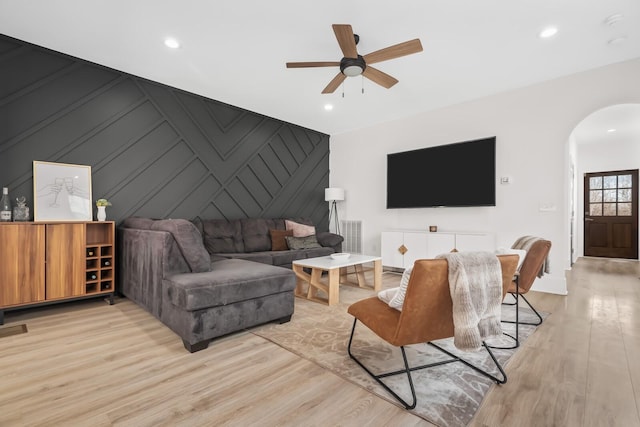 living area featuring arched walkways, recessed lighting, an accent wall, a ceiling fan, and light wood-type flooring