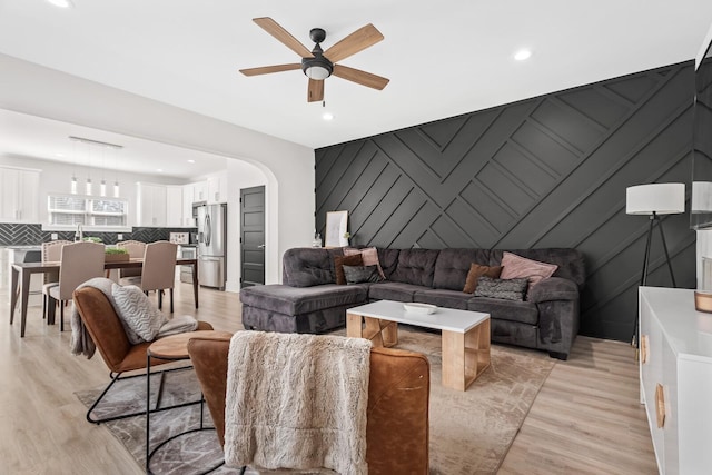 living area with arched walkways, recessed lighting, light wood-style flooring, an accent wall, and ceiling fan