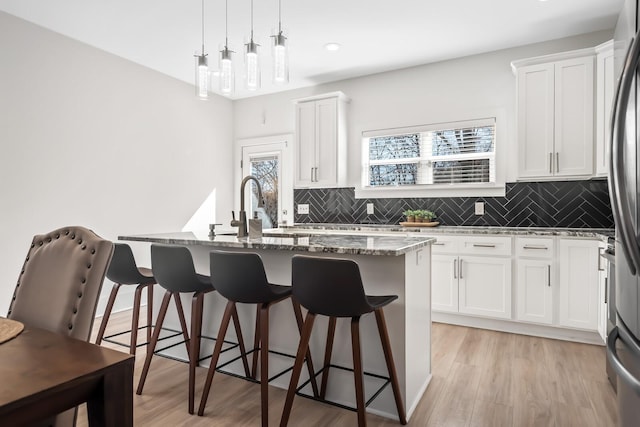 kitchen featuring a breakfast bar area, stone countertops, light wood-style floors, tasteful backsplash, and a center island with sink