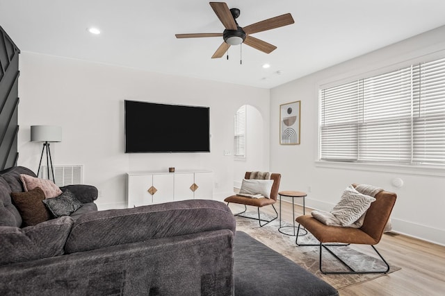 living room featuring arched walkways, ceiling fan, light wood-style flooring, visible vents, and baseboards