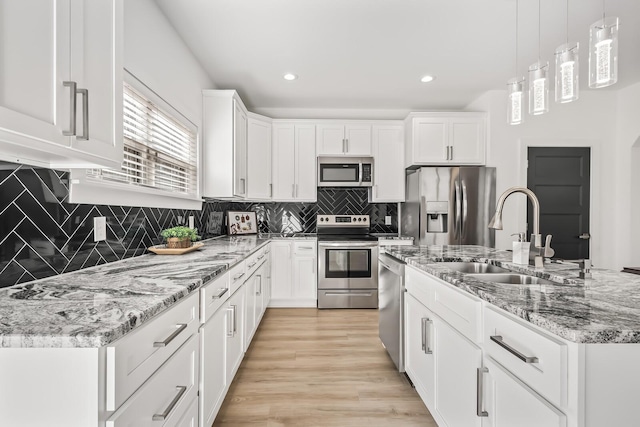 kitchen featuring decorative light fixtures, a center island with sink, appliances with stainless steel finishes, white cabinetry, and a sink