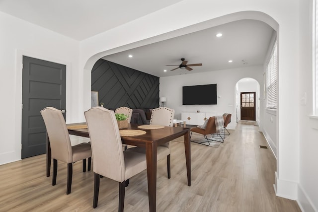 dining area with arched walkways, light wood-type flooring, and recessed lighting