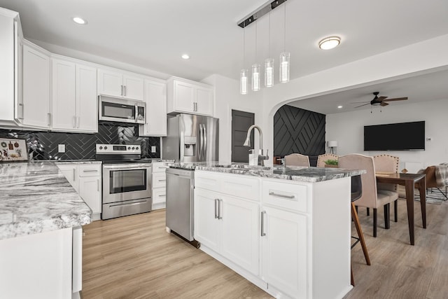 kitchen with stainless steel appliances, a sink, light wood finished floors, and decorative backsplash