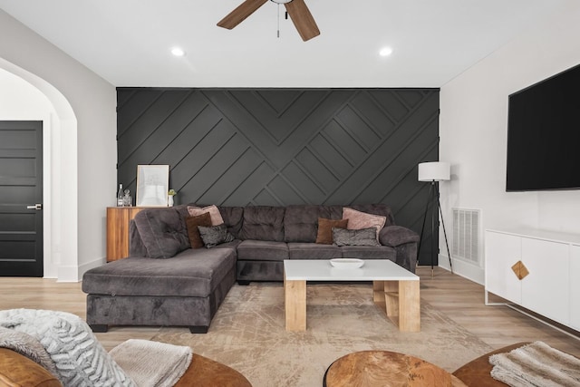 living room with light wood finished floors, an accent wall, visible vents, and arched walkways