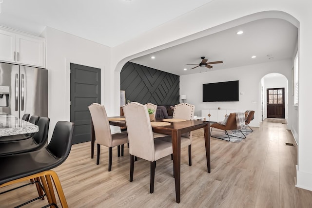 dining room with arched walkways, recessed lighting, an accent wall, a ceiling fan, and light wood-type flooring