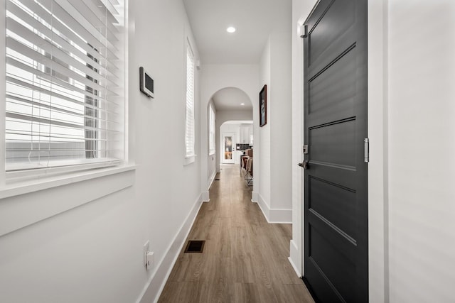 hall featuring baseboards, visible vents, arched walkways, wood finished floors, and recessed lighting