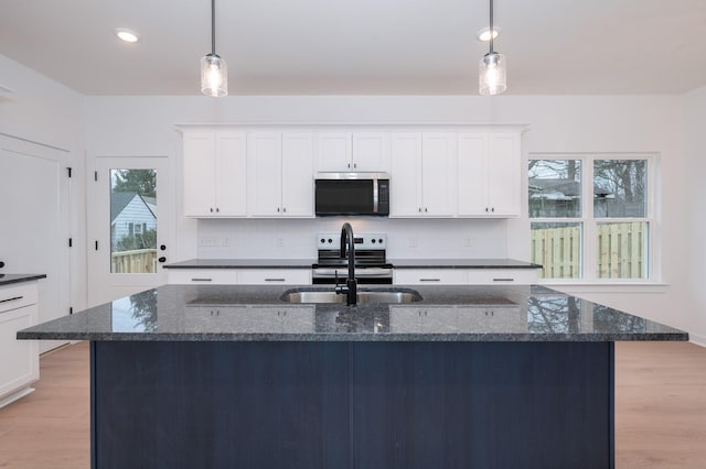 kitchen with white cabinetry, hanging light fixtures, appliances with stainless steel finishes, an island with sink, and dark stone counters