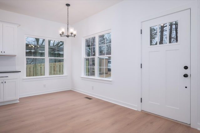 unfurnished dining area with a notable chandelier, a wealth of natural light, and light wood-type flooring